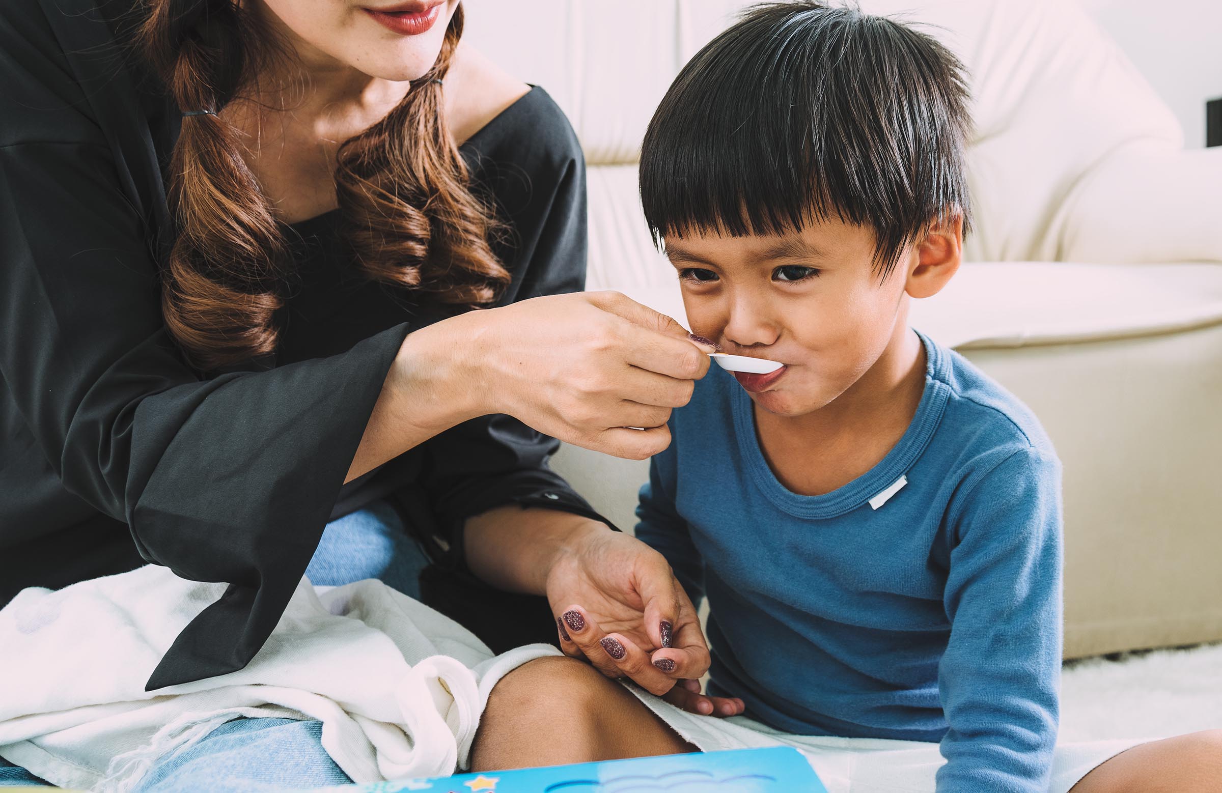 Mother giving child medication by spoon.