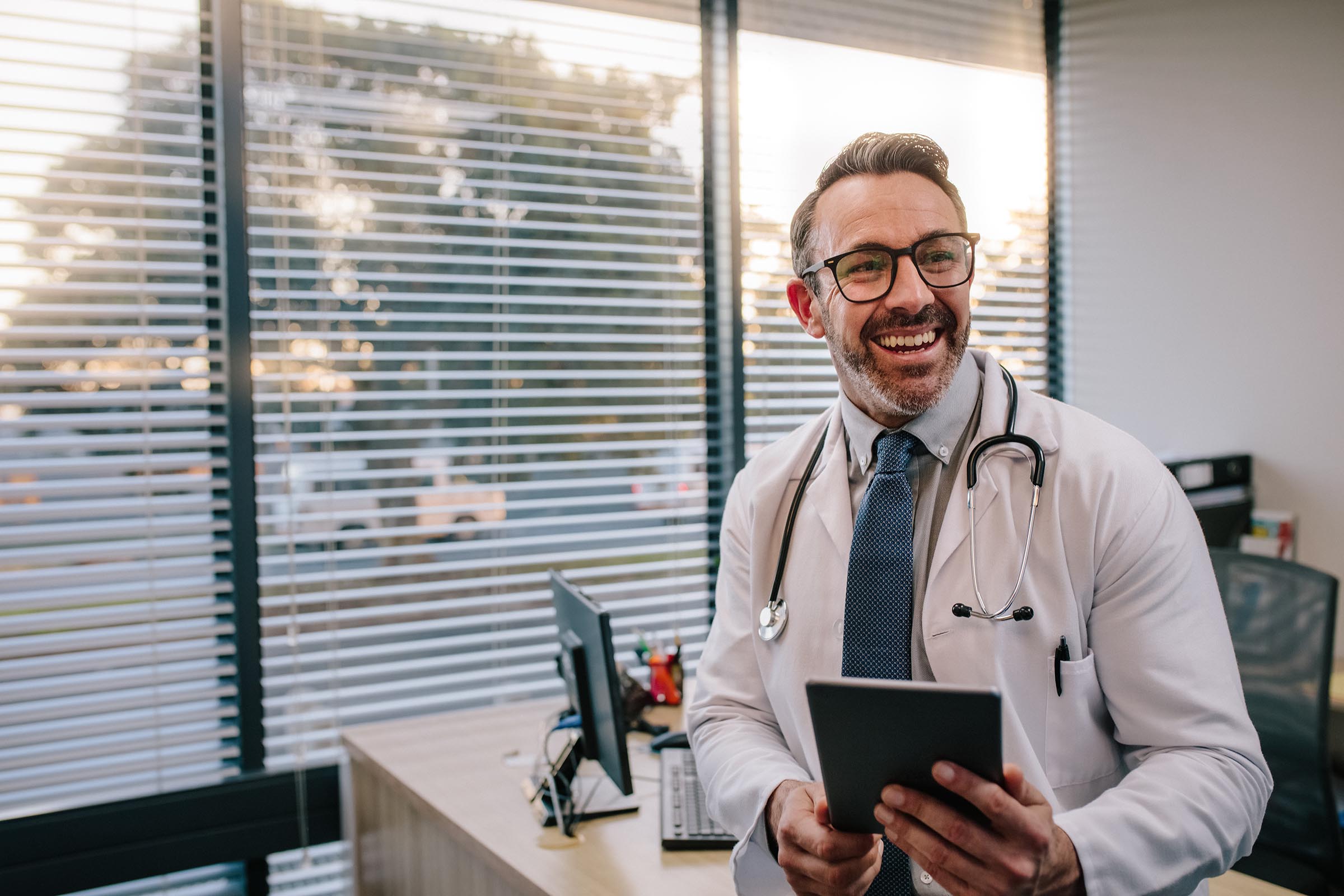 Doctor smiling with digital tablet in his office.