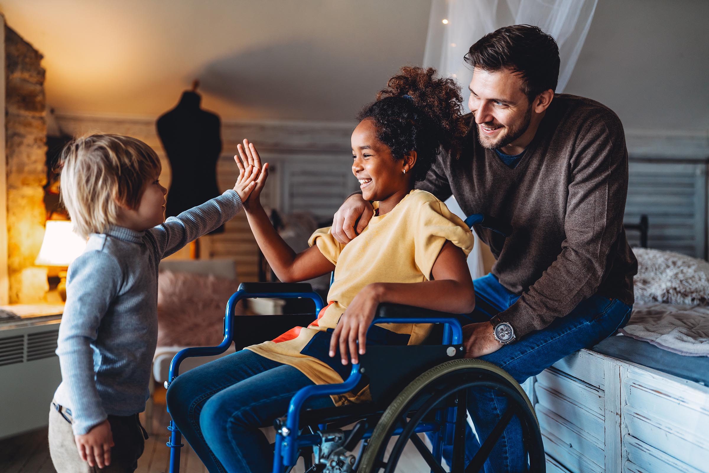 Smiling young child and older child in wheelchair with Dad