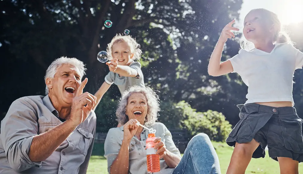 laughing grandparents blow bubbles with their grandchildren